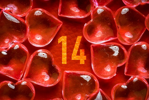 Transparent glass hearts on a red leather background with an inscription 14