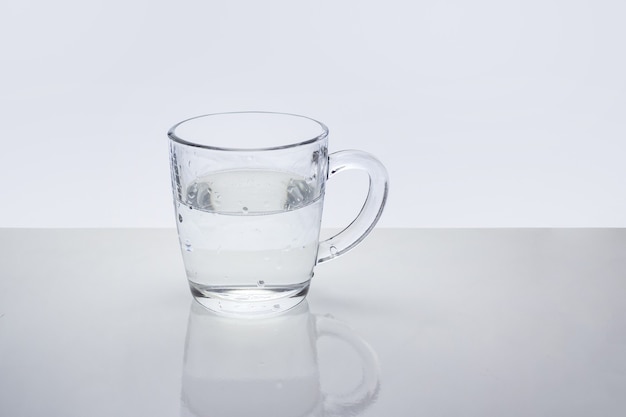 Transparent glass mug with water on light reflective surface.