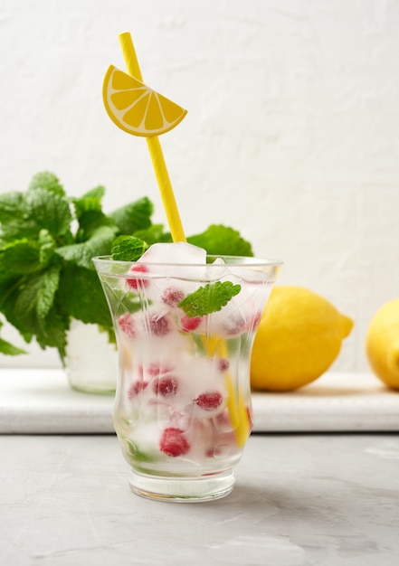 Transparent glass with lemonade and pieces of ice, red berries o