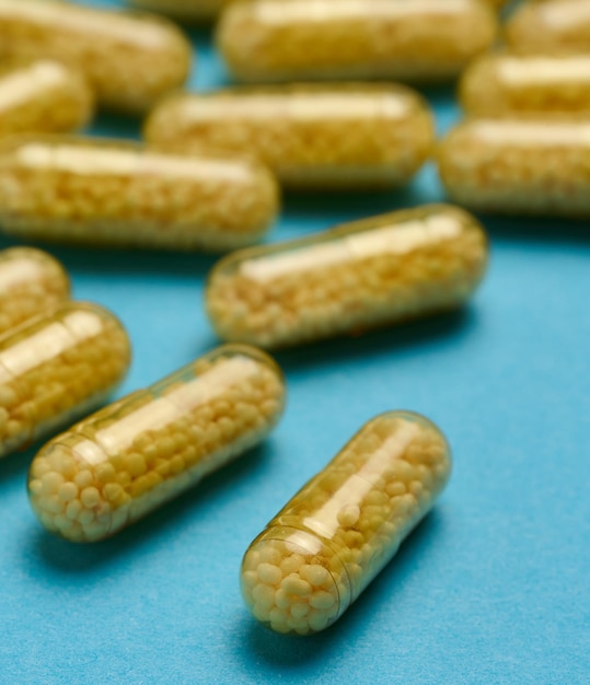 Transparent medical capsules with yellow granules inside on a blue background tablets for treatment vitamins