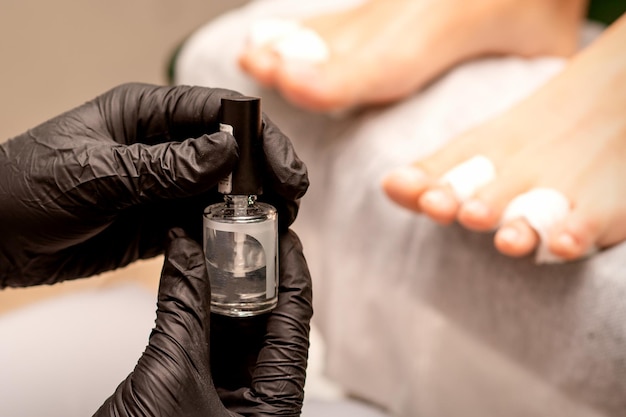 Transparent nail polish in the hands of a manicure master while painting nails on a female feet