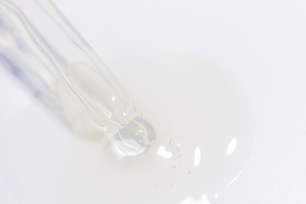 Transparent pipette with gel or liquid flowing out on a light background