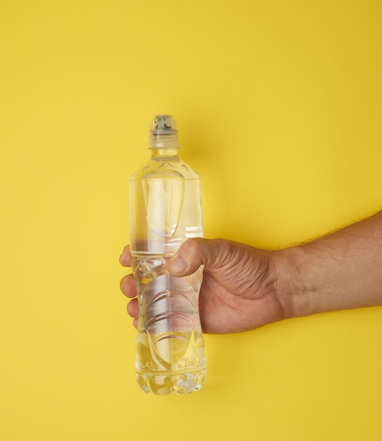 Transparent plastic bottle with fresh water in a male hand on a yellow