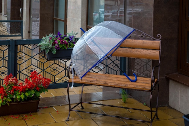 A transparent umbrella lies on a bench in the rain on a city street Climate weather