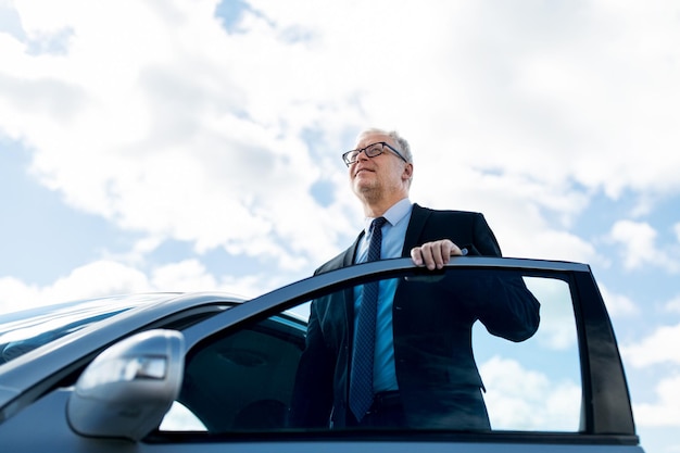 transport, business trip and people concept - senior businessman getting into car