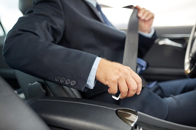 transport, business trip, safety and people concept - senior businessman fastening seat belt before driving car