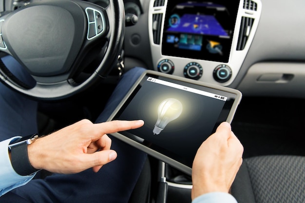 transport, business trip, technology, innovation and people concept - close up of male hands holding tablet pc computer with light bulb icon on screen in car