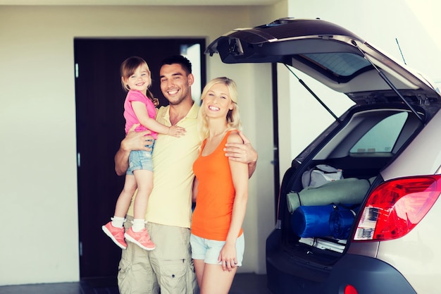 transport, leisure, road trip, travel and people concept - happy family with little girl packing things hatchback car at home parking space