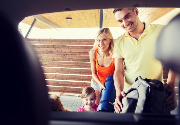 transport, leisure, travel, road trip and people concept - happy family packing things into car at home parking