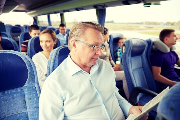 Photo transport, tourism, trip and people concept - senior man reading newspaper in travel bus