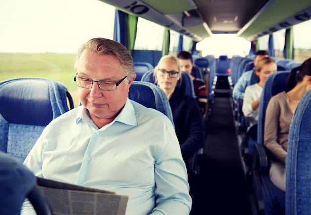 Photo transport, tourism, trip and people concept - senior man reading newspaper in travel bus