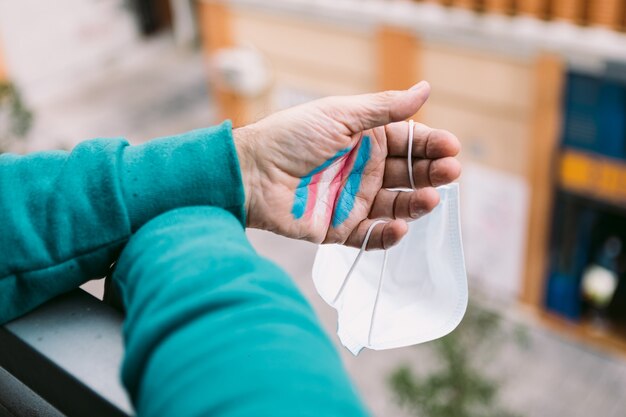 Transsexual man shows his hand with the painted transsexual flag, holding a FPP2 mask