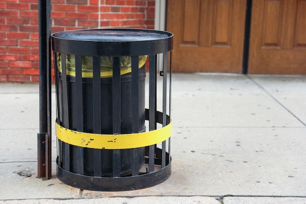 A trash can with a yellow band is on the sidewalk.