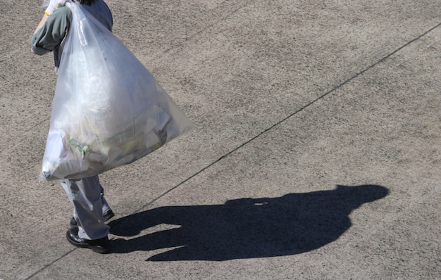 Photo a trash keeping worker carrying a plastic trash bag on sunny day.