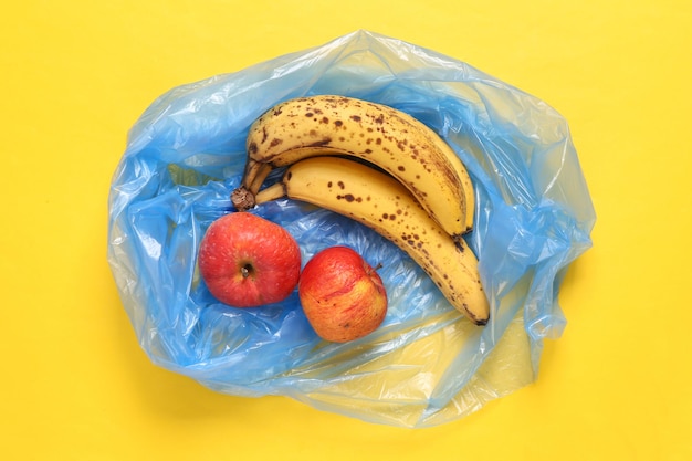 Trash packege with spoiled apples and bananas on yellow background