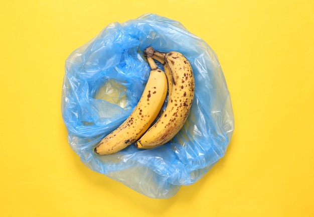 Trash packege with spoiled bananas on yellow background