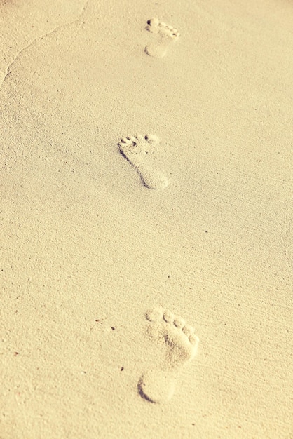 travel, adventure and beach concept - footprints on sand