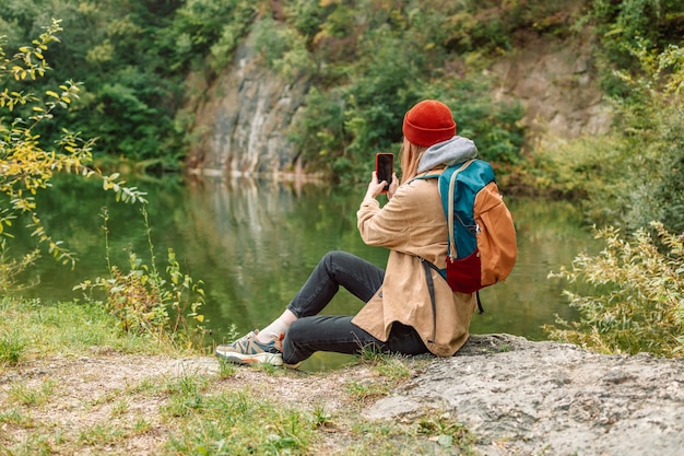 Travel adventure woman taking smart phone with mobile phone for Instagram photograph on mountain lake enjoying beautiful nature landscape