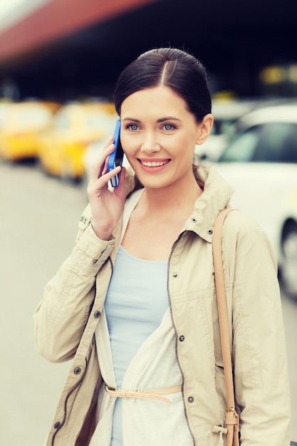 travel, business trip, people and tourism concept - smiling young woman calling and talking on smartphone over taxi station or city street