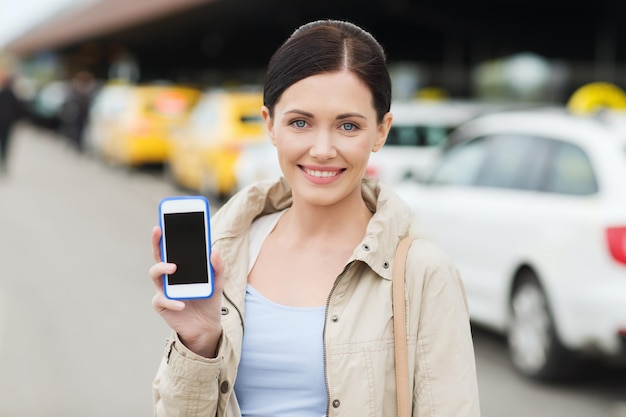 travel, business trip, people and tourism concept - smiling young woman showing smartphone blank screen over taxi station or city street