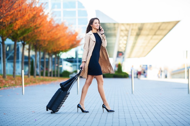 Travel. Business Woman in airport talking on the smartphone while walking with hand luggage in airport going to gate.