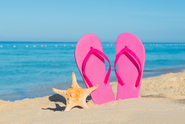 Travel by sea. Beach vacation. Pink flip-flops and starfish on sandy seashore.