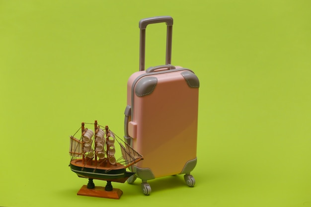 Travel concept. Mini plastic travel suitcase and ship on green background. Minimal style