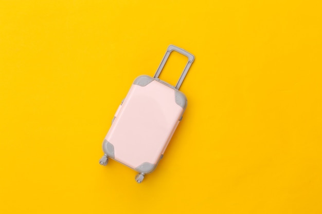 Travel concept. Mini plastic travel suitcase on yellow background. Minimal style. Top view, flat lay