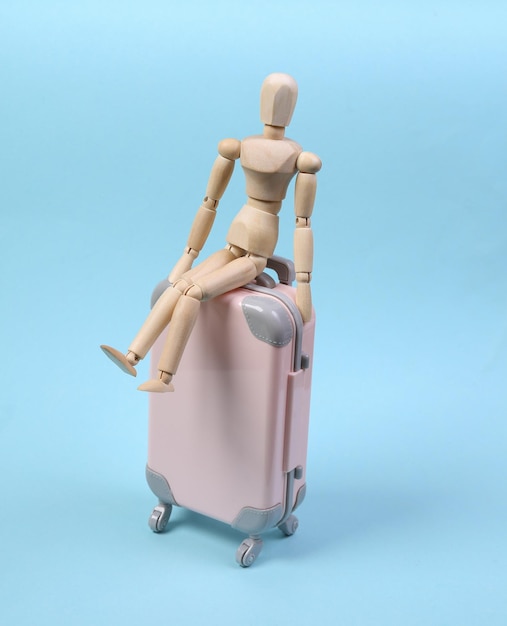 Travel concept. Wooden puppet sits on a travel suitcase on blue background