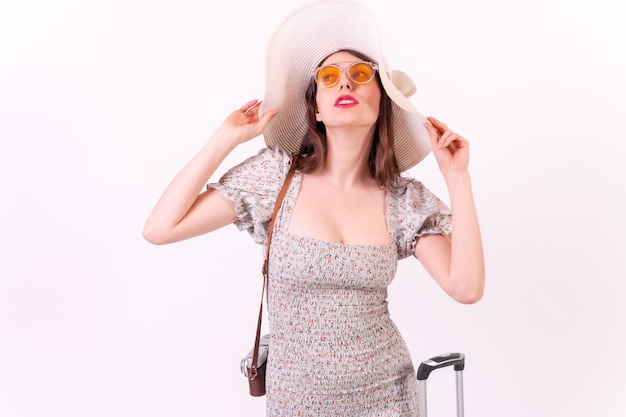 Travel concept Young tourist woman with suitcase and hat in a fashion portrait on a white background