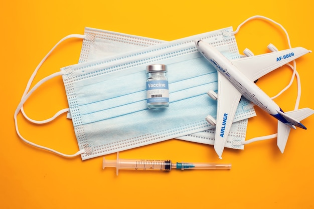 Travel during covid-19 pandemic. Airplane model, protection medical masks, vaccine and syringe on yellow background. Healthcare and medicine concept.