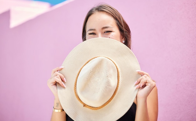 Travel fashion and summer hat with a woman tourist in the city on a pastel color pink wall background Happy holiday and tourist with a female traveler covering her face with a sunhat in town