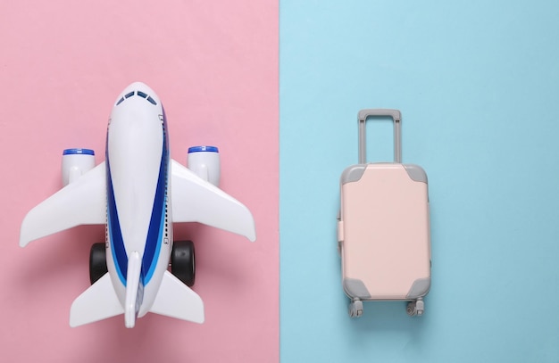 Travel flat lay Toy passenger plane and luggage on a bluepink pastel background Top view