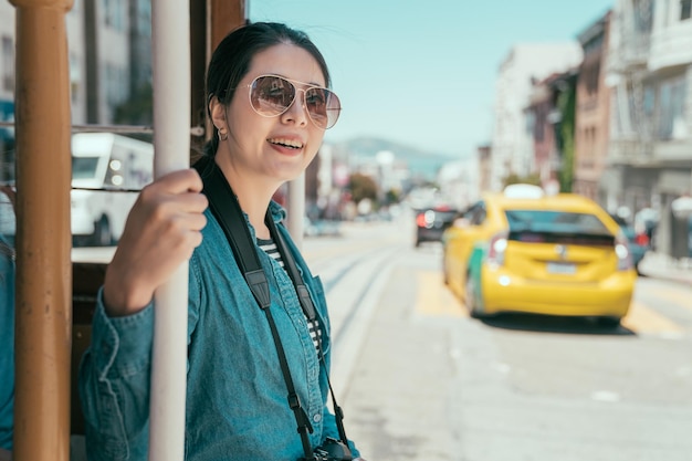 travel girl passengers enjoy ride in cable car in San Francisco. mechanical public transport concept. young woman tourist in sunglasses smiling holding hand rail outdoor sightseeing on tramway.