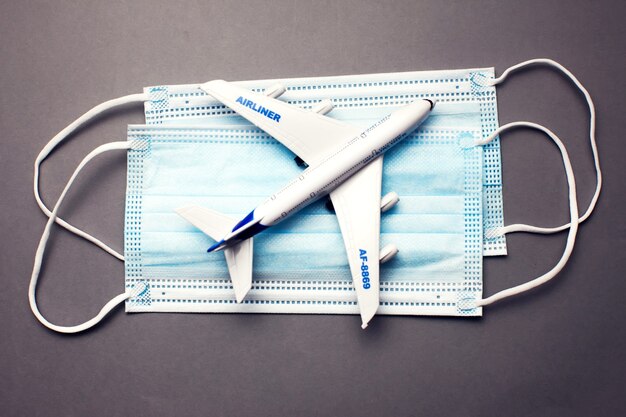 Travel and health concept during covid-19 pandemic. Model of a white plastic airplane and masks on grey background.