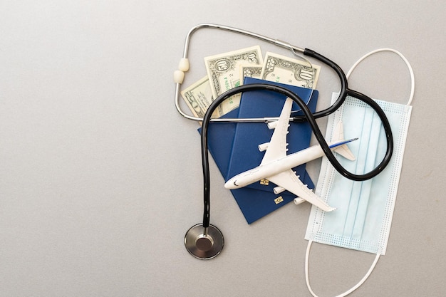 Photo travel and healthcare concept. top view of face mask, hand sanitizer, passport, stethoscope and toy plane isolated on blue background with copy space.