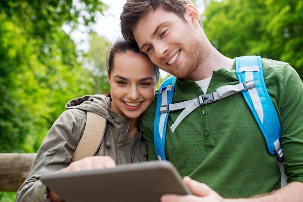 travel, hiking, backpacking, tourism and people concept - smiling couple with backpacks and tablet pc computer in nature