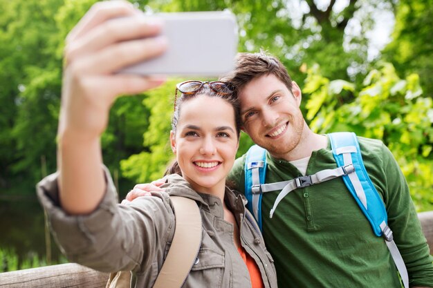 travel, hiking, backpacking, tourism and people concept - smiling couple with backpacks taking selfie by smartphone in nature