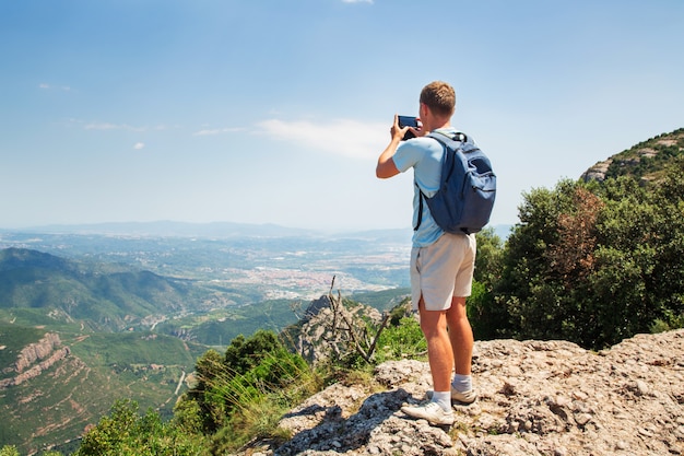 Travel man with backpack standing take a photo by smartphone Mountians Sunny day Copy space