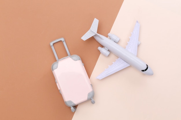 Travel minimalism. Mini plastic travel suitcase and air plane on beige brown background. Minimal style. Top view, flat lay