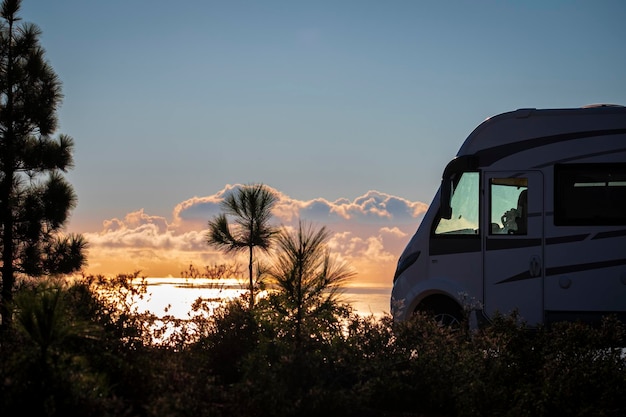 Travel people lifestyle and nomadic life with white camper van motorhome and beautiful colorful sunset on the ocean in background. Travel and enjoy freedom and nature with rv