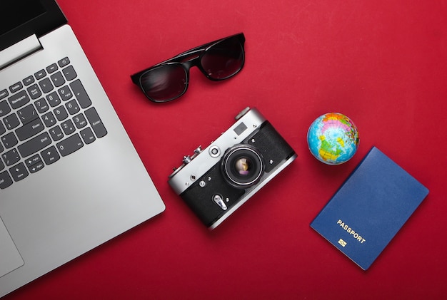 Travel still life. Online booking. Laptop, tourist accessories on a red background. Travel around the world