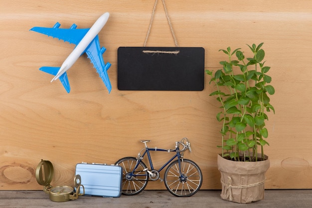 Travel time concept blank blackboard airplane model little bicycle and suitcase compass on wooden background