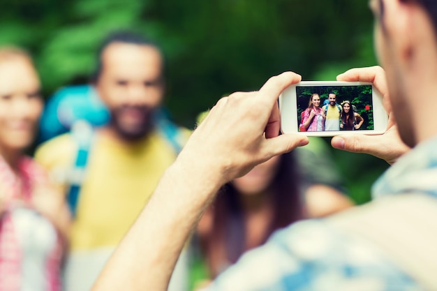 travel, tourism, hike, technology and people concept - close up of man photographing friends with backpacks by smartphone outdoors