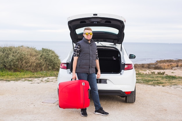 Travel, tourism and people concept. happy man in glasses standing with red suitcase