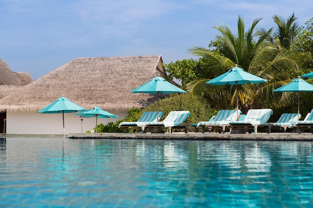 travel, tourism, vacation and summer holidays concept - parasol and sunbeds over sea and sky on maldives beach