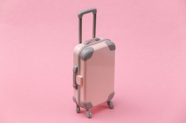 Travel or trip concept. Mini plastic travel suitcase on pink background. Minimal style