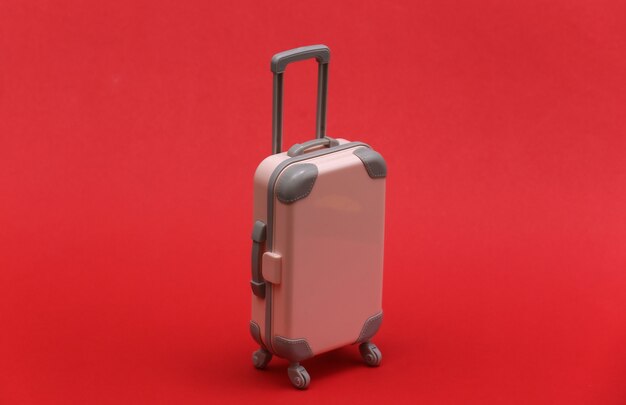 Travel or trip concept. Mini plastic travel suitcase on red background. Minimal style