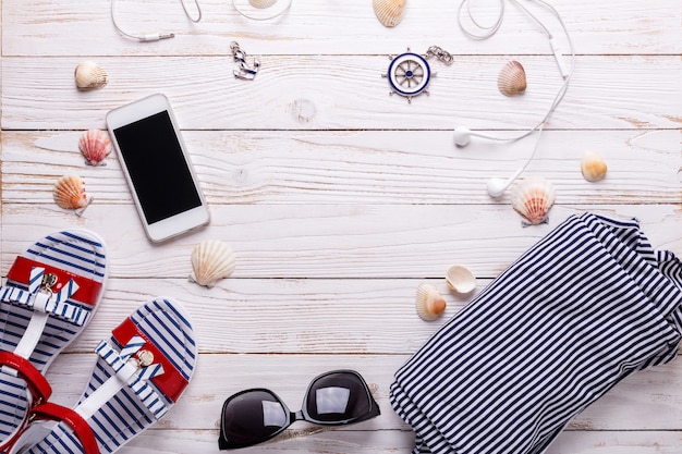 Travel vacation concept with sandals, headphones, sunglasses, smartphone, seashells and striped t-shirt.