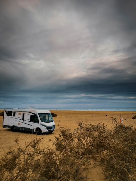 Travel vacation lifestyle with camper parked at the beach with sea view- Recreational vehicle camping car camp in the nature. Holiday concept transport big van free with ocean and sky in background